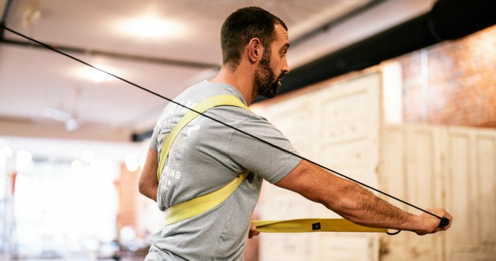 athlete patient at physical therapy in gray t-shirt working on machine to recover from most common shoulder injuries in sports