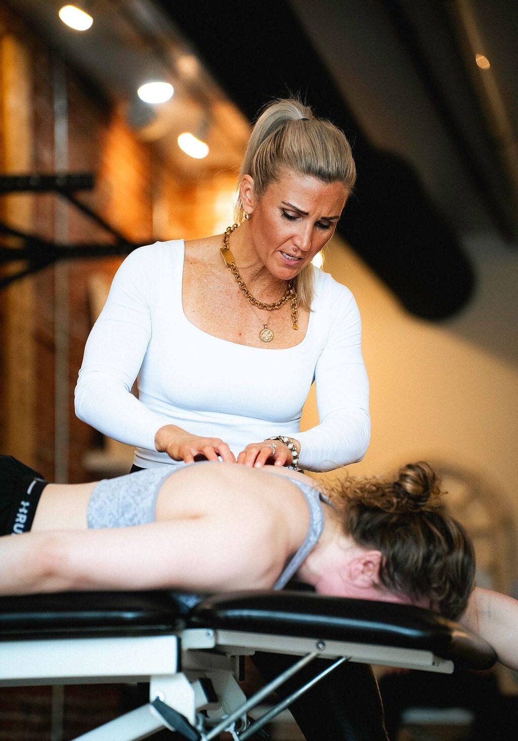 Female physical therapist performing manual therapy on a patient’s back while they lie face down on a treatment table in a clinic.
