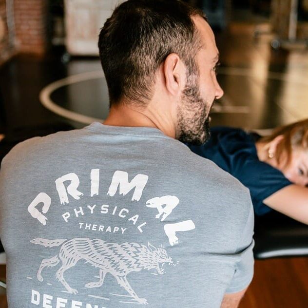 a man with primal physical therapy shirt performing a session with a woman laying on the bench