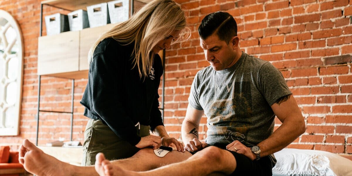 Dr. JJ is performing therapy on a patient with a knee injury. The patient is lying on an examination table while Dr. JJ gently manipulates the knee joint, providing careful and attentive treatment to aid in the patient's recovery.